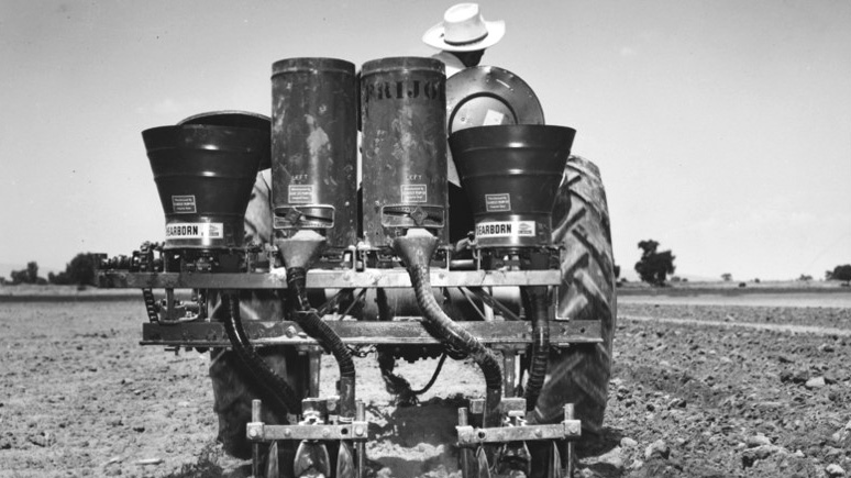 Black and white image of an experimentation station. Equipment in being driven by a person wearing a white hat.