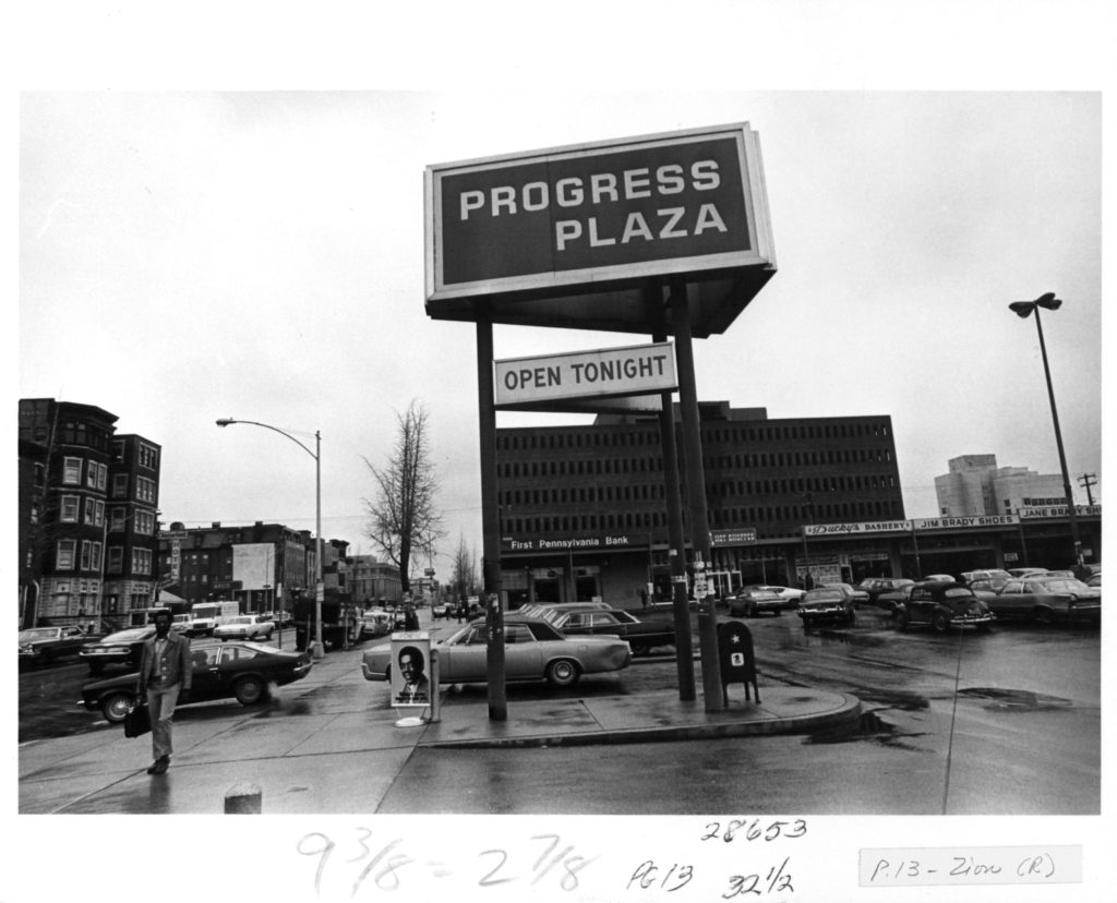Black and white image of signage that reads "Progress Plaza" at the entrance of the shopping center.