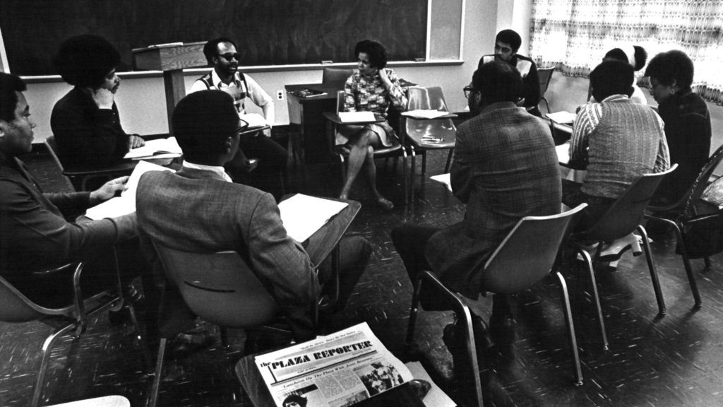 Black and white image of local residents sitting around a large table discussing the start-up capital for Progress Plaza.