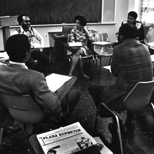 Black and white image of local residents sitting around a large table discussing the start-up capital for Progress Plaza.