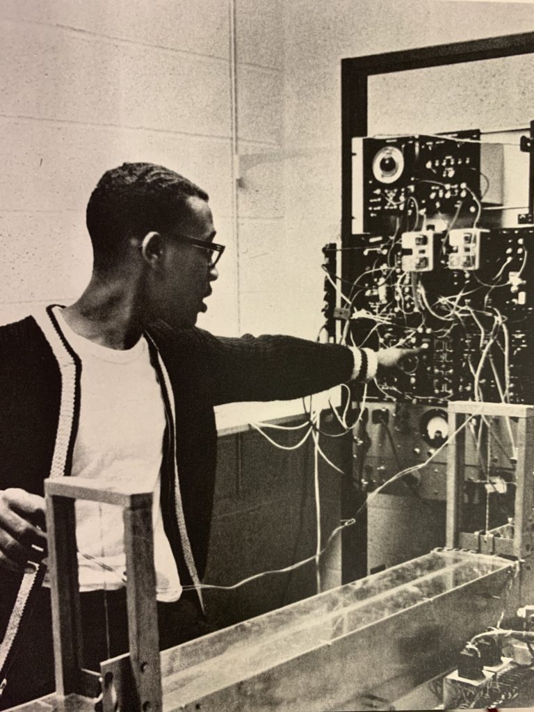 A young man pointing towards a device covered in wires of different lengths.
