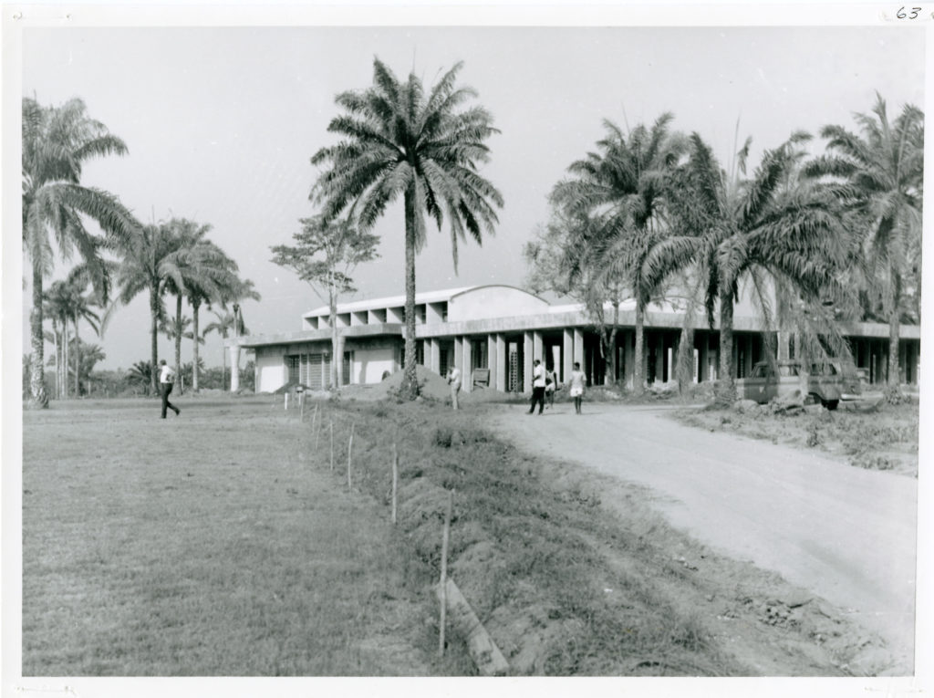 Photo of crop-drying site in Nigeria. The one story building is located under palm trees.