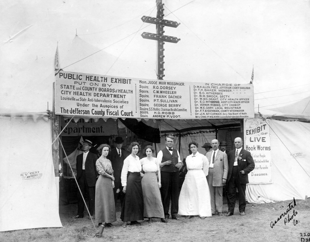 Black and white image of a group of visiting doctors and microscopists standing in front of a Public Health Exhibit tent in Louisville.