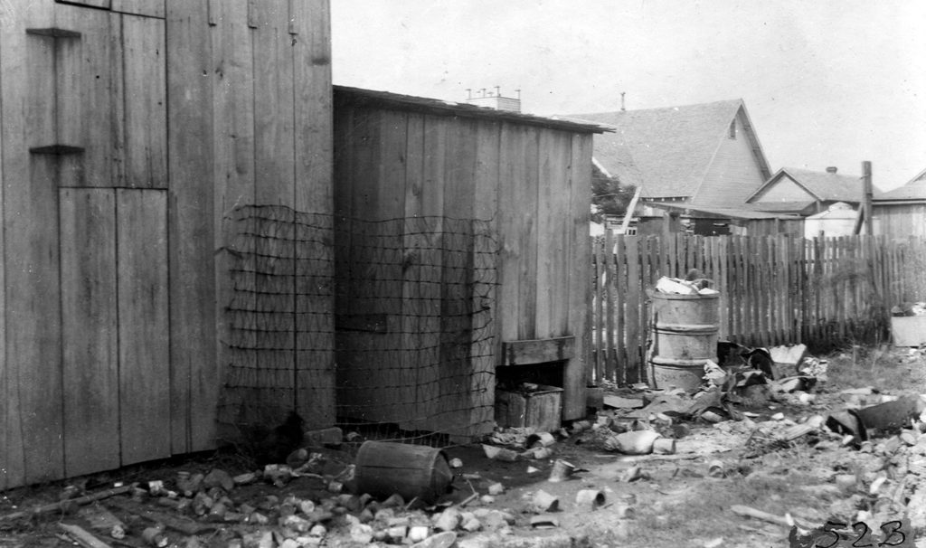 Black and white image of unsanitary conditions with garbage lining the back of sheds.