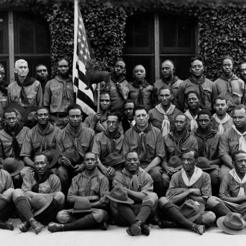 Black African American Boy Scout Leaders (Scoutmasters) pose for a photograph, sitting in rows with an American flag
