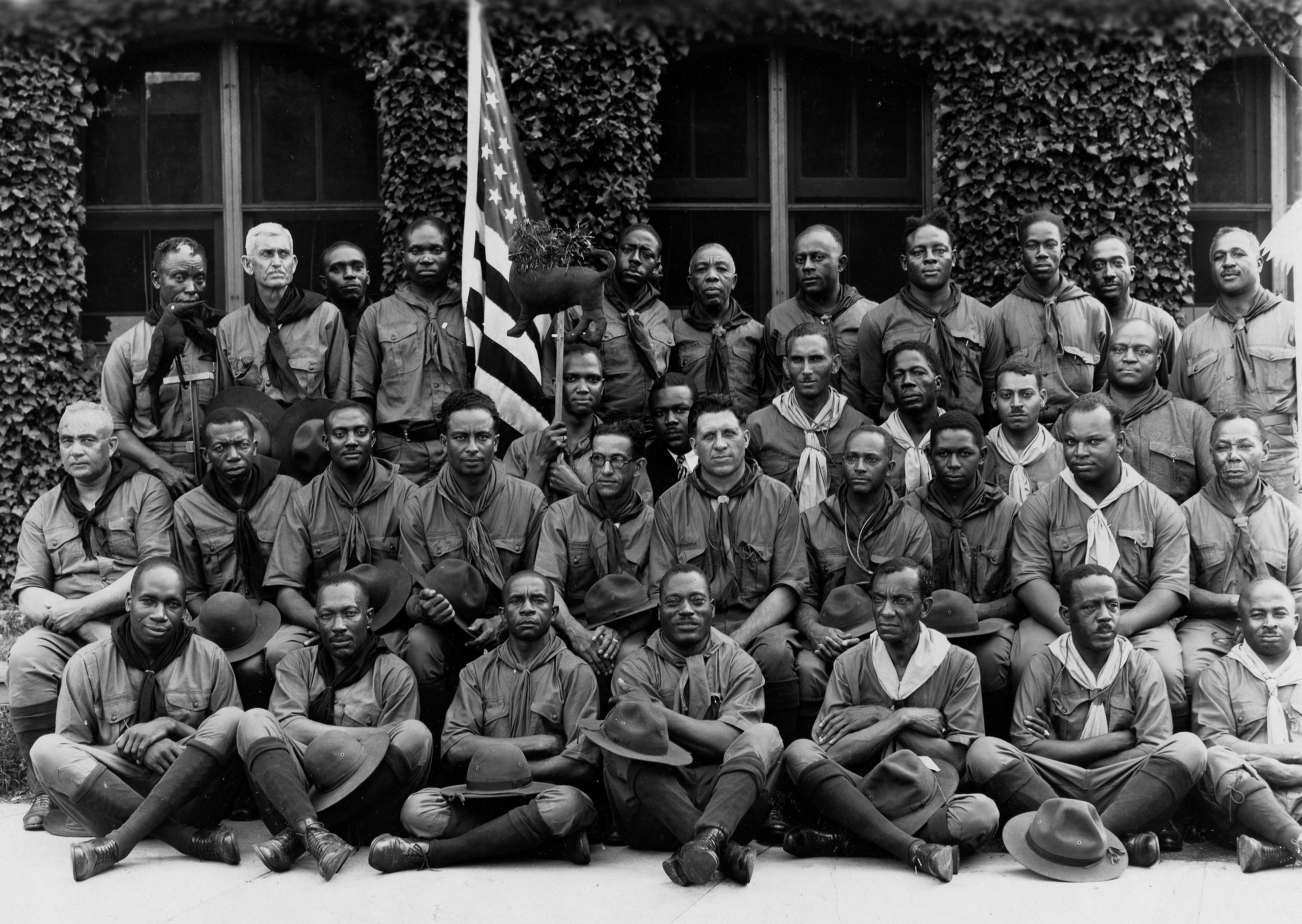 Black African American Boy Scout Leaders (Scoutmasters) pose for a photograph, sitting in rows with an American flag