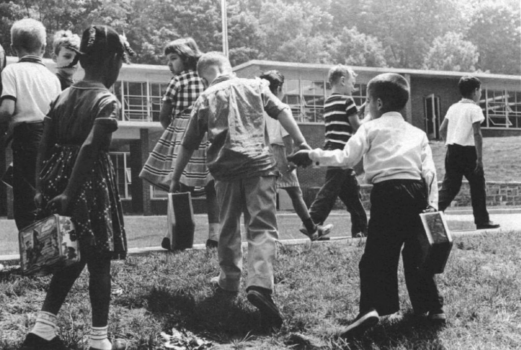 Elementary children of diverse ethnic backgrounds get ready to go inside their school, two hold hands