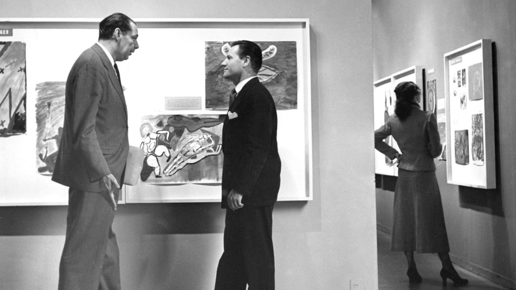 Black and white photo of Nelson as president of the MoMa standing with Rene d'Harnoncourt in front of art exhibits.