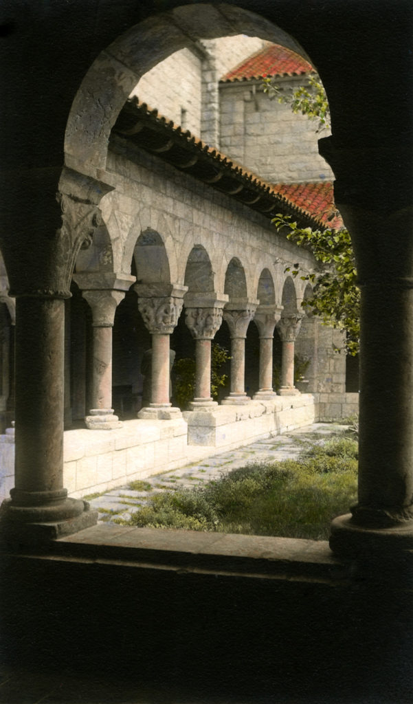Photo of gothic columns looking towards the courtyard in the Met Cloisters. Featured is red roofing upon the building.