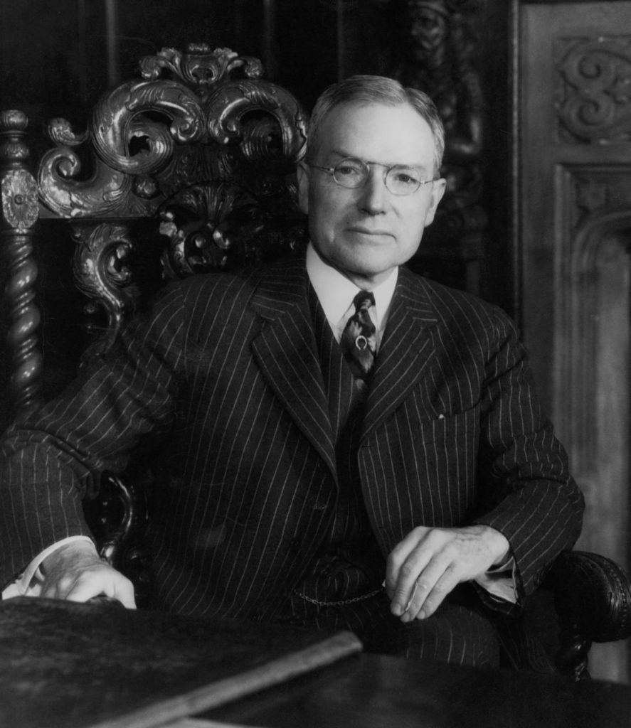 Portrait of John D. Rockefeller, Jr. dressed in a black pinstripe suit and sitting in a chair