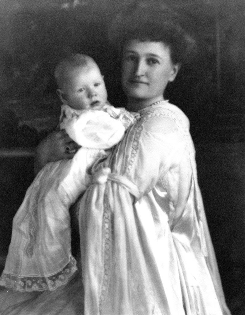 Black and white photo of Abby and Nelson in 1908. Nelson is dressed in a long gown, as Abby is holding him.