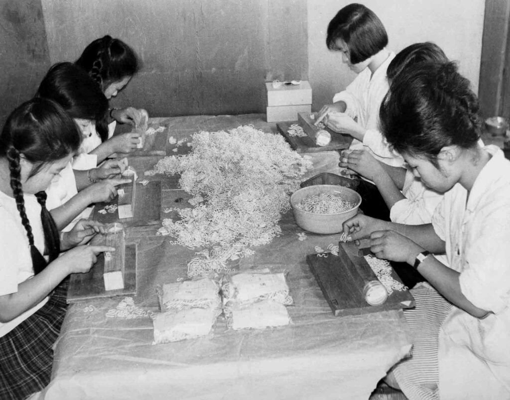 Six young Korean women seated at a table making IUD loops.