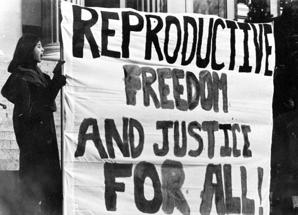 Protest for reproductive rights. Unidentified student holds sign reading "Reproductive freedom and justice for all!" on Low Steps, circa 1980s-90s.